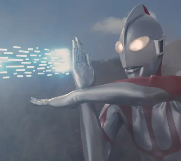 Ultraman, a silver and red robot-like figure, emits blue energy beams from its hand against a cloudy sky and mountain backdrop, conveying action and power.