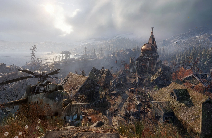 A desolate village under a cloudy sky with a crashed helicopter in the foreground in Metro Exodus. Rustic buildings and a distant, weathered church create an eerie, abandoned feel. Metro 4