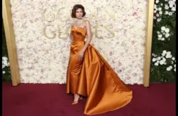 Zendaya posing for cameras at a show in a long, pumpkin orange dress, with matching high heel shoes.