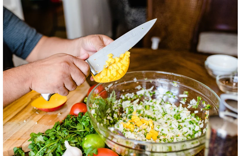 A man cutting up a fresh mango to add to his pico de gallo