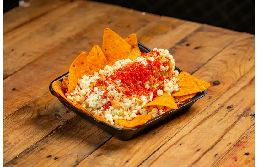 A bowl of festive street corn dip with tortilla chips.
