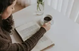 In the daily devotional, a young woman sits with an open Bible and coffee reading.