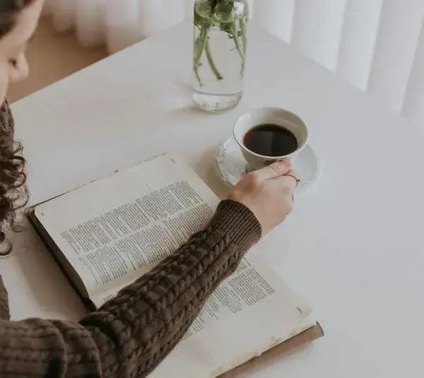 In the daily devotional, a young woman sits with an open Bible and coffee reading.