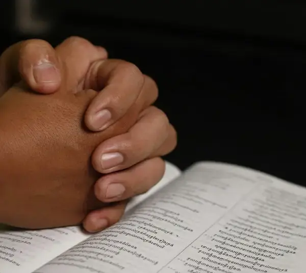 In daily devotion, a person's hands folded in prayer over a Bible are shown.