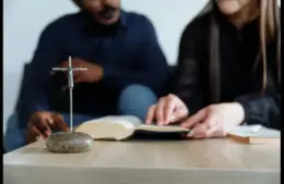 In the daily devotional, two people are studying the Bible. near a replica of the cross.