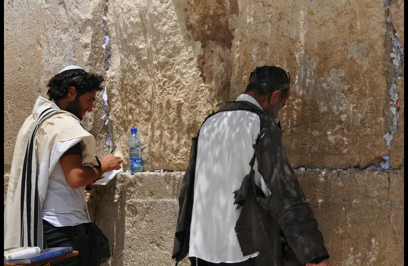In daily devotional, religious men are saying prayers beside a wall.