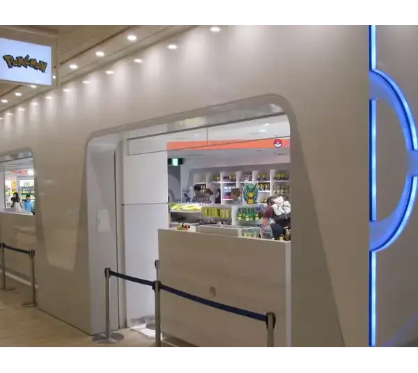 A sleek, modern Pokémon Centers exterior with blue neon accents and a white facade resembling a train. Interior shelves display colorful merchandise. Bright, clean ambiance. The Pokémon Company