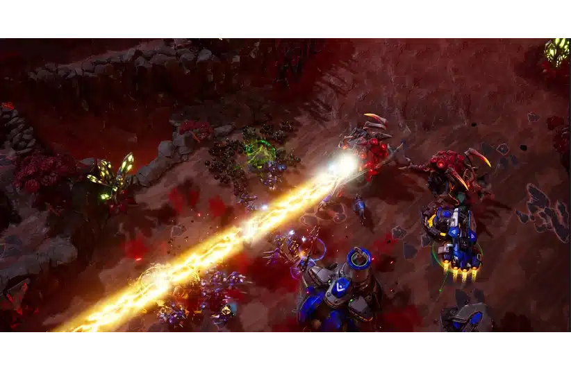 Aerial view of a Stormgate battle scene with robotic units fighting. A bright yellow laser beam cuts through the center, surrounded by vivid explosions.