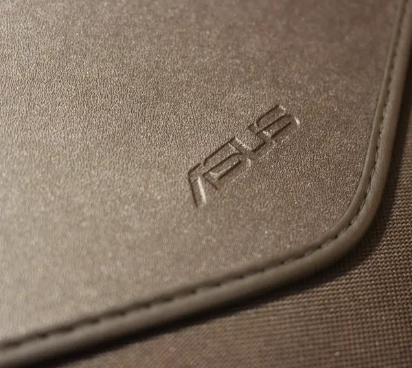 Close-up of a textured brown leather case with the "ASUS" logo embossed, conveying a sleek and professional appearance.