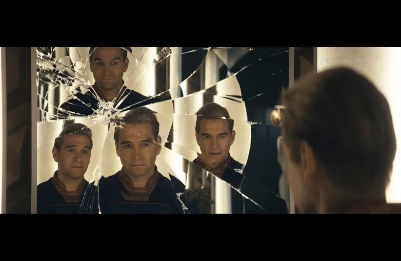 Antony Starr in The Boys gazes into a broken mirror, his reflection fragmented into multiple images. The scene conveys tension and introspection.