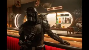 Pedro Pascal in "Star Wars: The Mandalorian and Grogu (2026)" stands confidently at a dimly lit bar, carrying a small, green, big-eared creature on their shoulder. The setting is futuristic and warm.