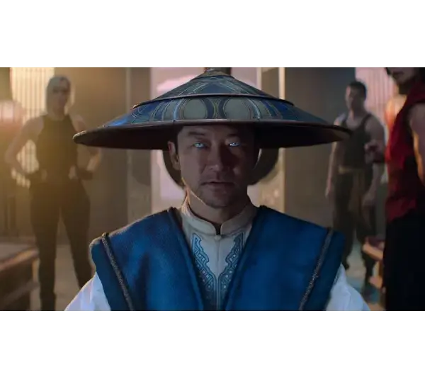 Tadanobu Asano in Mortal Kombat 2 (2026), in a blue robe and wide-brimmed hat, stares intently, his eyes glowing blue. Three people stand behind him in a dimly lit room, creating a tense atmosphere.