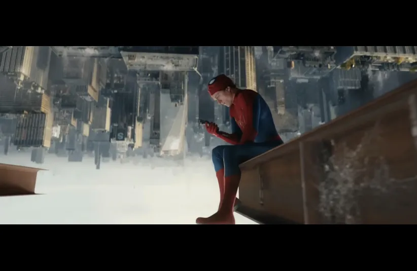 Spider-Man sits on the edge of a building, looking at a phone. The cityscape appears upside down below, creating a disorienting, contemplative scene.