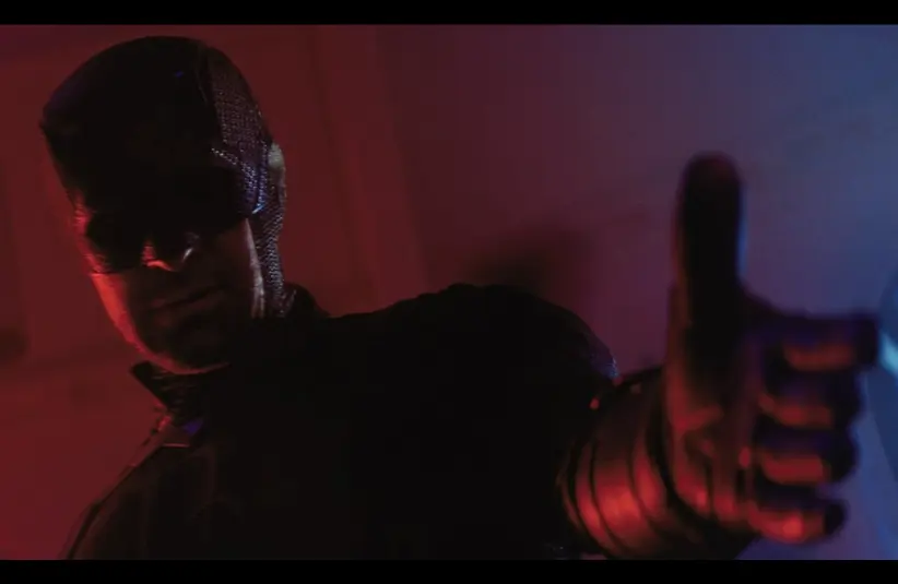 Daredevil, bathed in red and blue light reaches forward, conveying intensity and mystery. The atmosphere is dark and dramatic, highlighting action. (Daredevil Born Again)