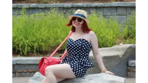 Sweetheart neckline dotted playsuit styled with a red bag, aviators, and a hat trimmed with a navy‑blue ribbon, showcasing chic polka dots effortlessly.