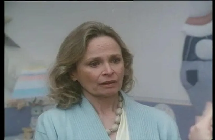 an image of Bonnie Bartlett in the tv series "St Elsewhere" with shoulder-length hair wears a light blue sweater and necklace, looking concerned.