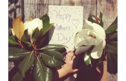 A child's hand holding flowers next to a "Happy Mother's Day" card