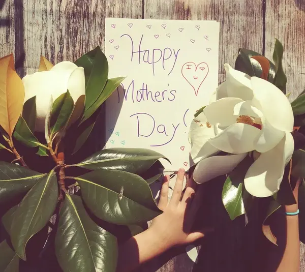 A child's hand holding flowers next to a "Happy Mother's Day" card