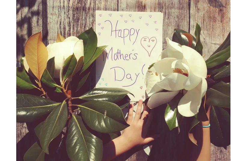 A child's hand holding flowers next to a "Happy Mother's Day" card