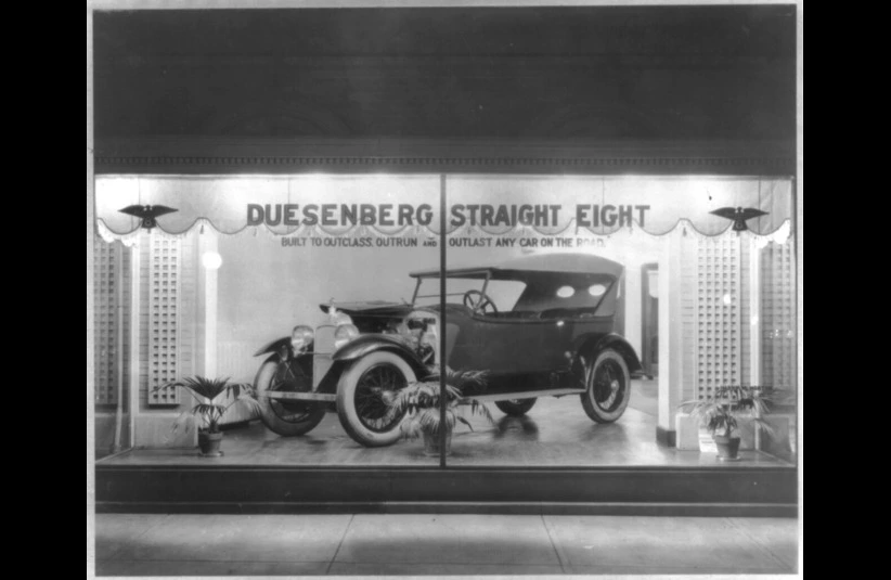 Vintage Duesenberg Straight Eight car displayed in a showroom window with elegant curtains and potted plants. Bold text advertises its superiority.
