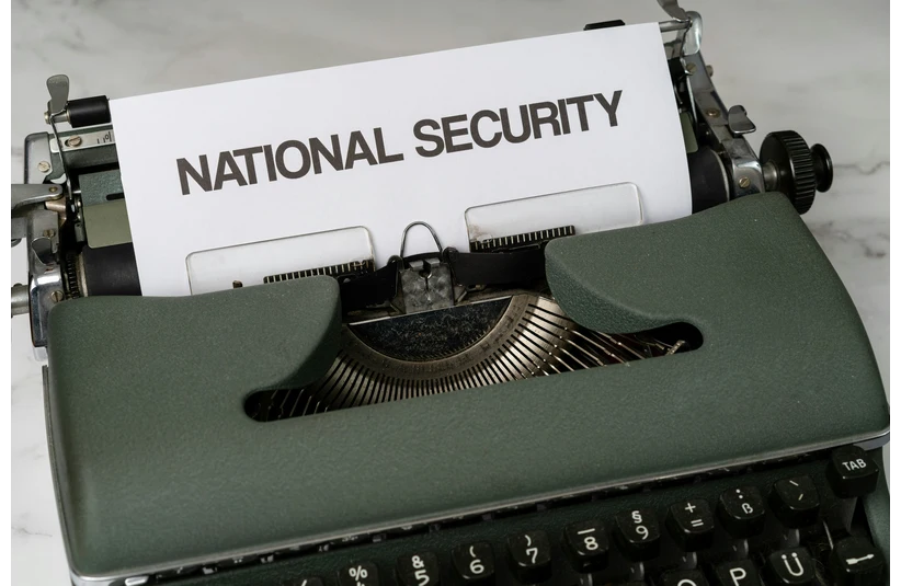 A green vintage typewriter with a white paper showing the words "NATIONAL SECURITY." The setup evokes a sense of importance and urgency.