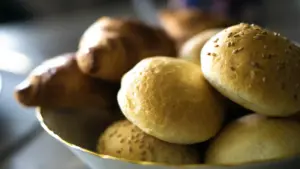 A bowl filled with various rolls and buns placed on a wooden table. Refined carbs, bread