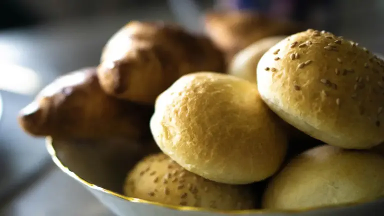 A bowl filled with various rolls and buns placed on a wooden table. Refined carbs, bread