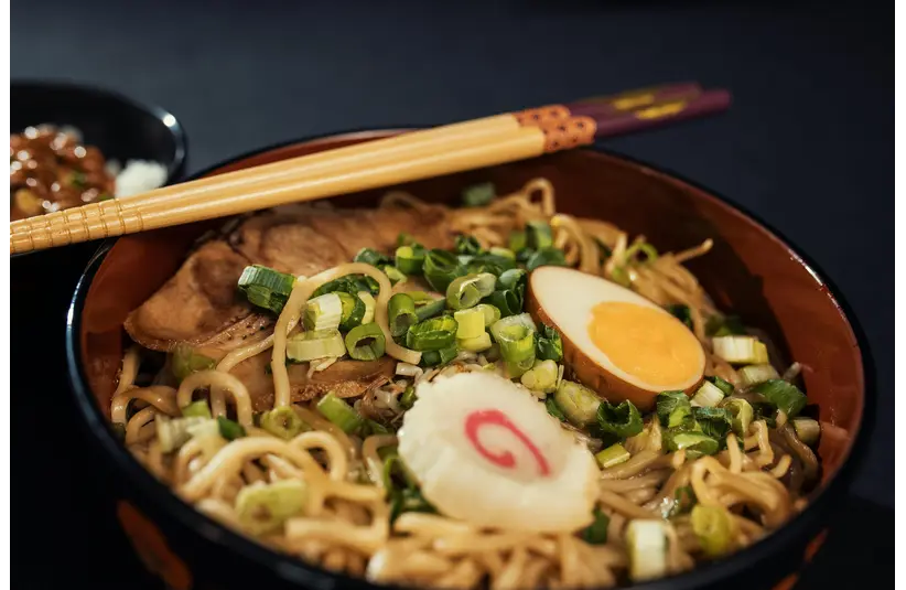 Bowl of traditional Japanese ramen with boiled egg, scallions, and narutomaki served with chopsticks perfect for quick meals.