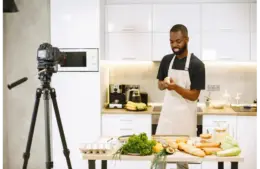 A man prepares food in a kitchen while recording a food content cooking video.