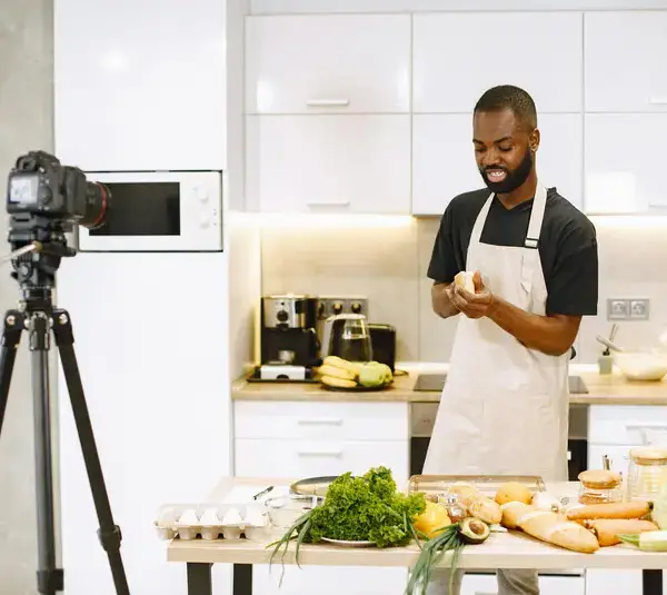 A man prepares food in a kitchen while recording a food content cooking video.