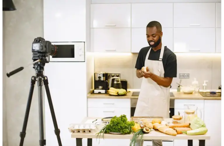 A man prepares food in a kitchen while recording a food content cooking video.