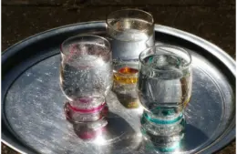 Three glasses of sparkling water with vibrant rims on a shiny metallic tray, catching sunlight.