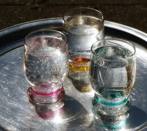 Three glasses of sparkling water with vibrant rims on a shiny metallic tray, catching sunlight.