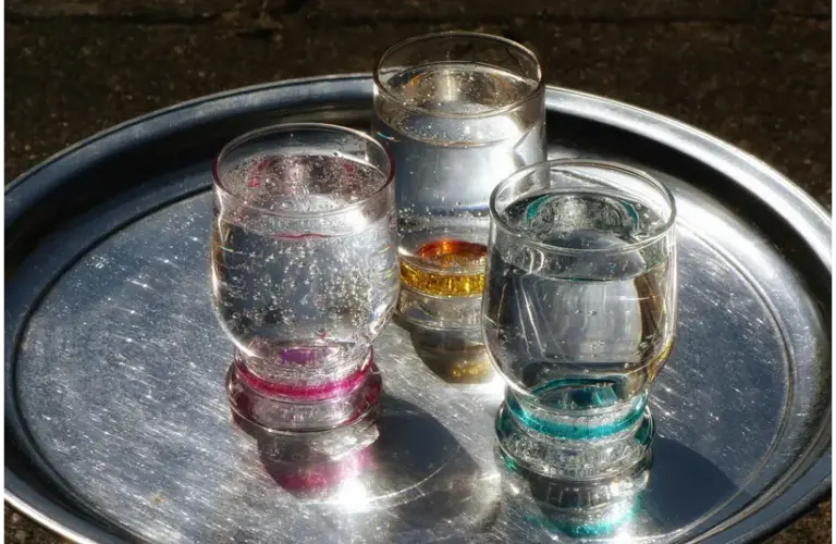 Three glasses of sparkling water with vibrant rims on a shiny metallic tray, catching sunlight.