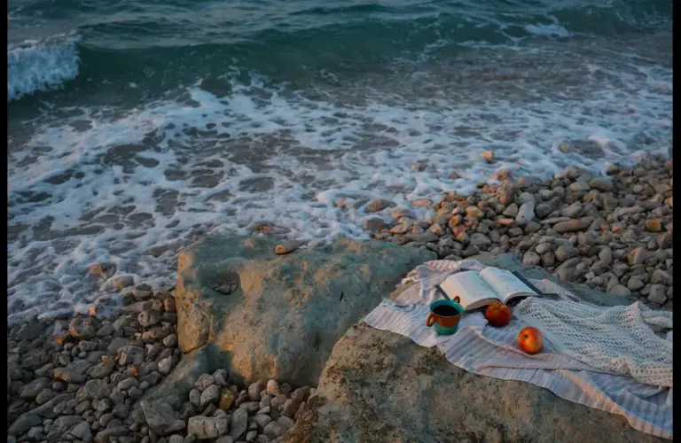 In daily devotional, a Bible is near the seaside along with other items indicatng relaxation and study.