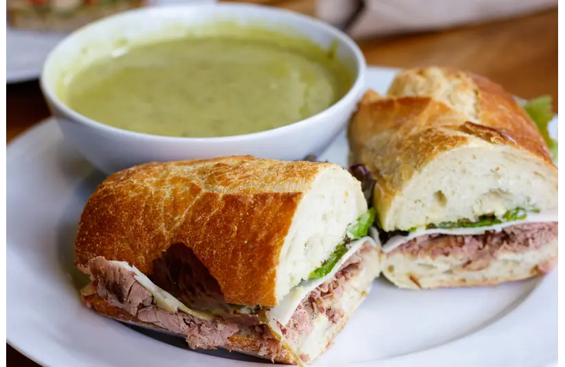 Close-up of sandwiches with meat and cheese paired with a bowl of green soup for budget dates.