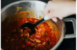 One of freshly cooked quick meals with tomatoes and spices in a pot, stirred by hand