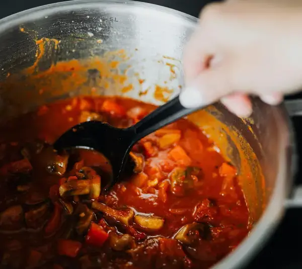 One of freshly cooked quick meals with tomatoes and spices in a pot, stirred by hand