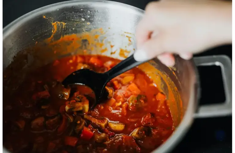 One of freshly cooked quick meals with tomatoes and spices in a pot, stirred by hand