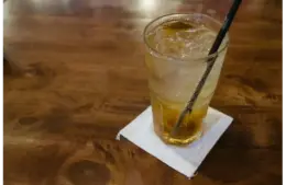 Glass of dirty soda with ice cubes on a wooden table, capturing a refreshing moment