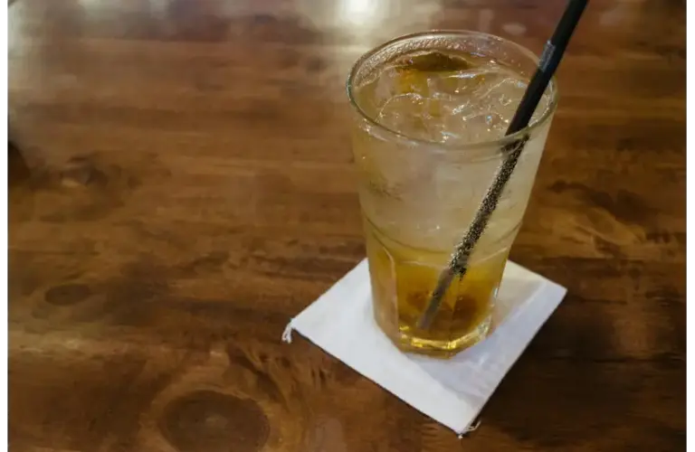 Glass of dirty soda with ice cubes on a wooden table, capturing a refreshing moment