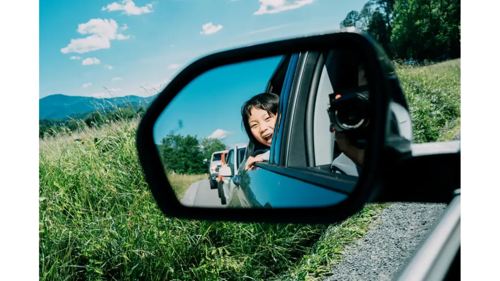 A smiling child looks out of a car’s side‑view mirror during a sunny adventure through lush greenery, capturing the carefree magic of road trips. Perhaps in a Ford.
