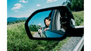 A smiling child looks out of a car’s side‑view mirror during a sunny adventure through lush greenery, capturing the carefree magic of road trips.