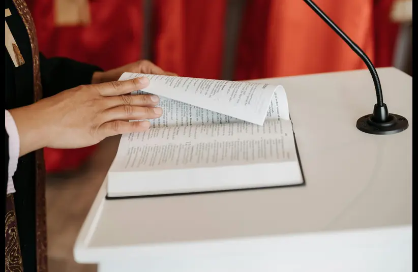 In daily devotional, a church leader is at podium turning pages of the Bible, which is God's counsel.
