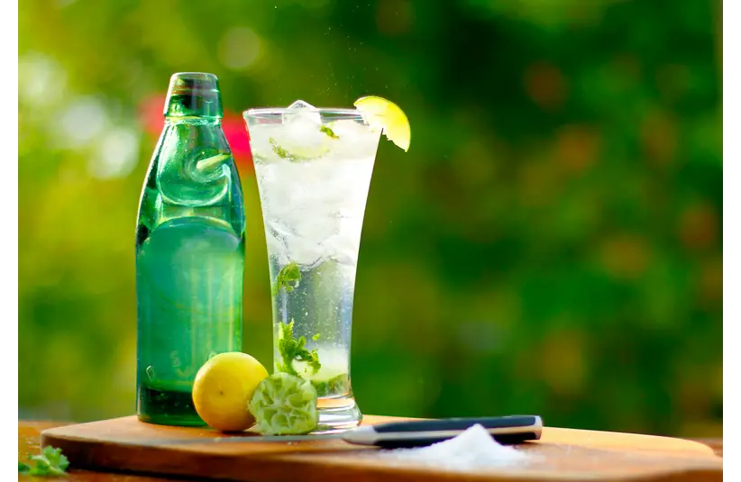 A tall glass of dirty soda with ice and citrus fruits on a sunny day
