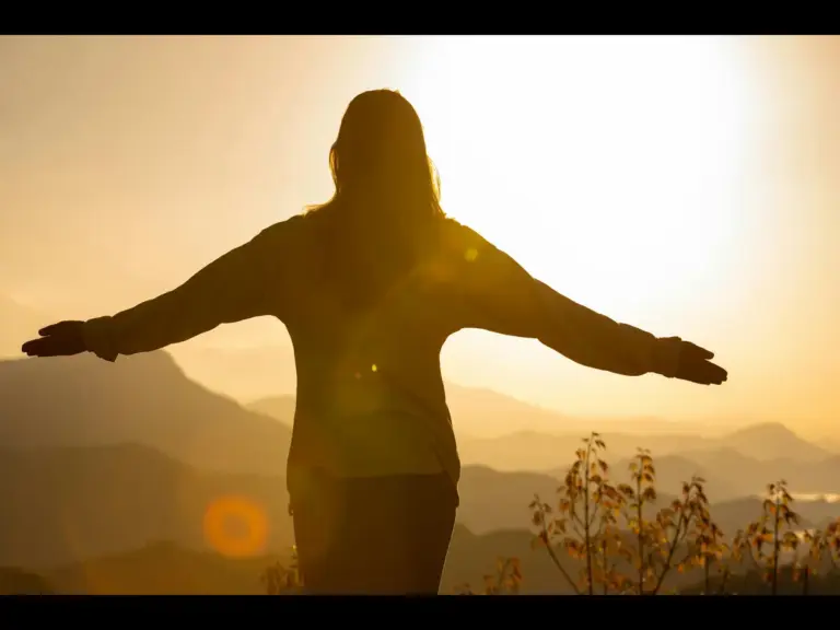 In daily devotional, a woman stands with her arms outstreched as though she's open to hearing God's voice.