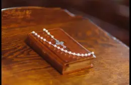 In daily devotional , a Bible is draped with a pearl necklace with a cross pendant.