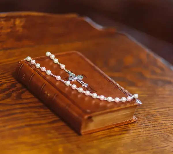 In daily devotional , a Bible is draped with a pearl necklace with a cross pendant.