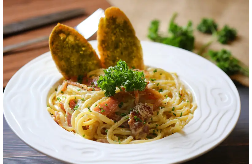 Delicious creamy carbonara pasta served with garlic bread on a stylish white plate for budget dates