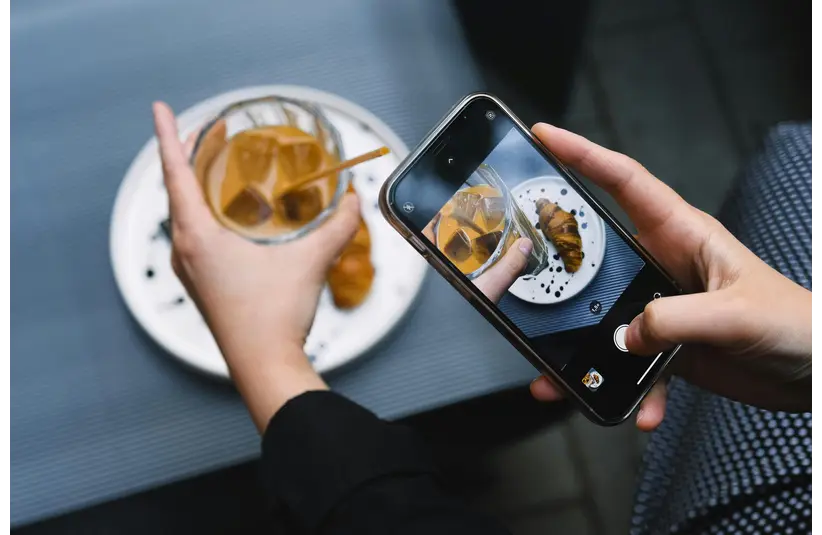 Hands taking a photo of iced coffee and croissant with a smartphone, perfect for food content bloggers.